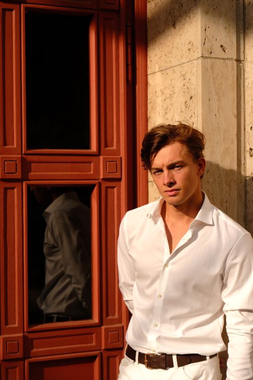 Free A stylish young man in white attire poses by a wooden door in Berlin. Stock Photo
