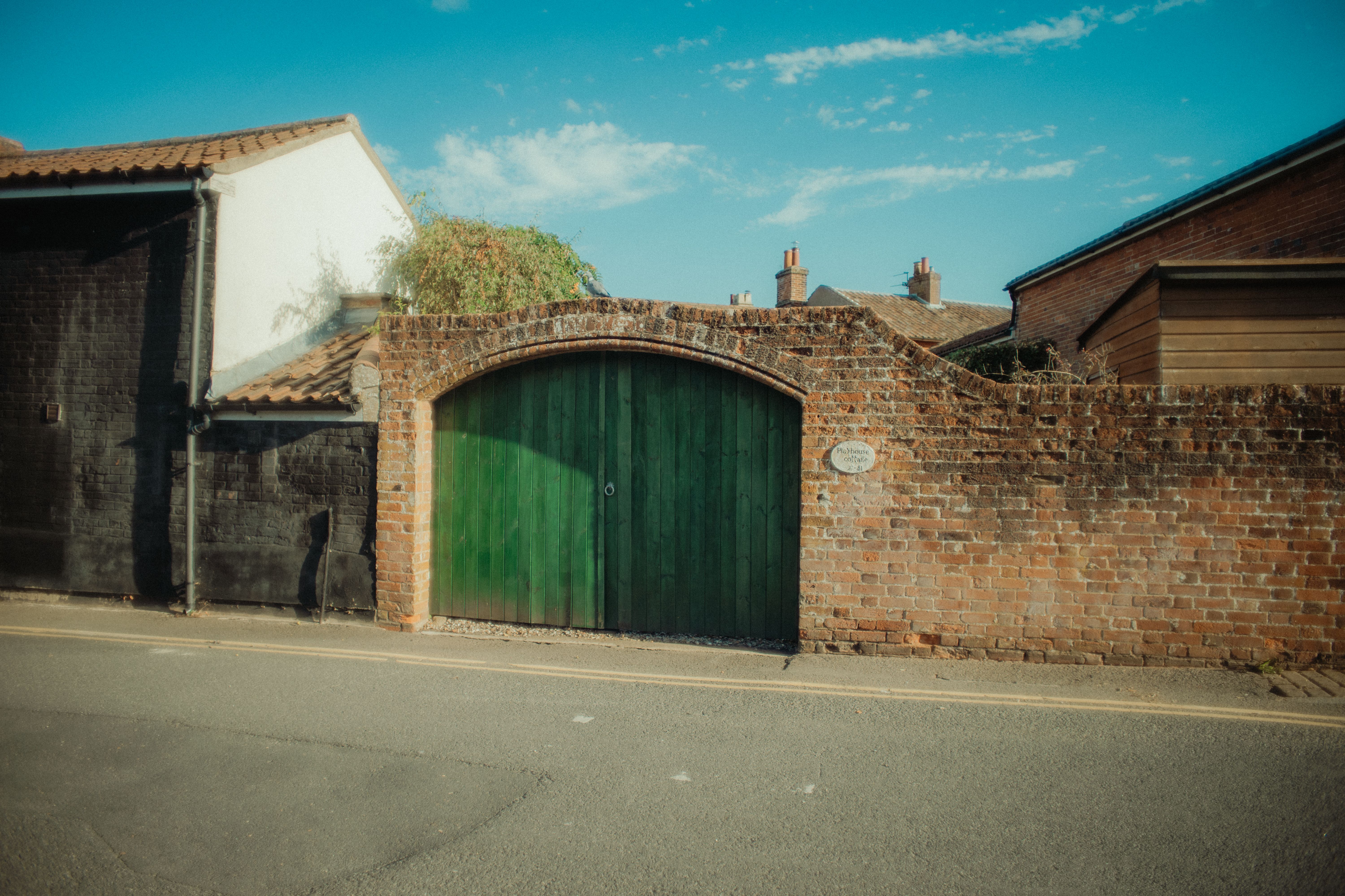 Vintage brick gate with a green door on a quiet street in Dereham, England.