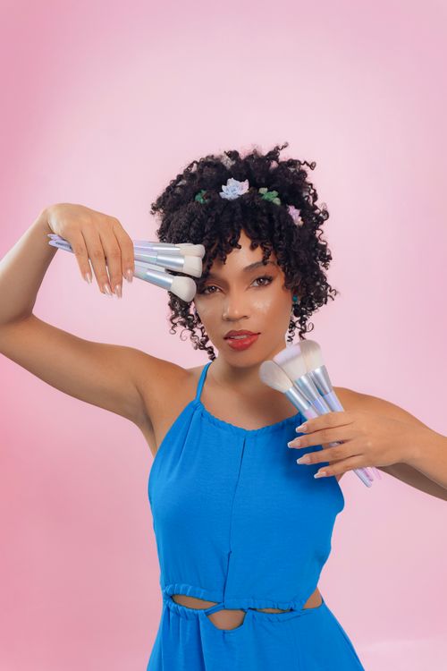 Free Elegant woman posing with makeup brushes against a pink background, showcasing beauty and style. Stock Photo