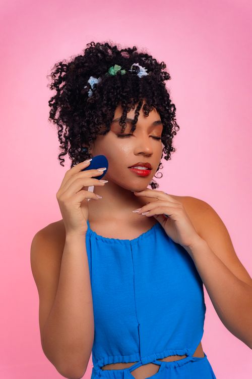 Free Charming woman with curly hairstyle holding a makeup sponge against a pink background. Stock Photo