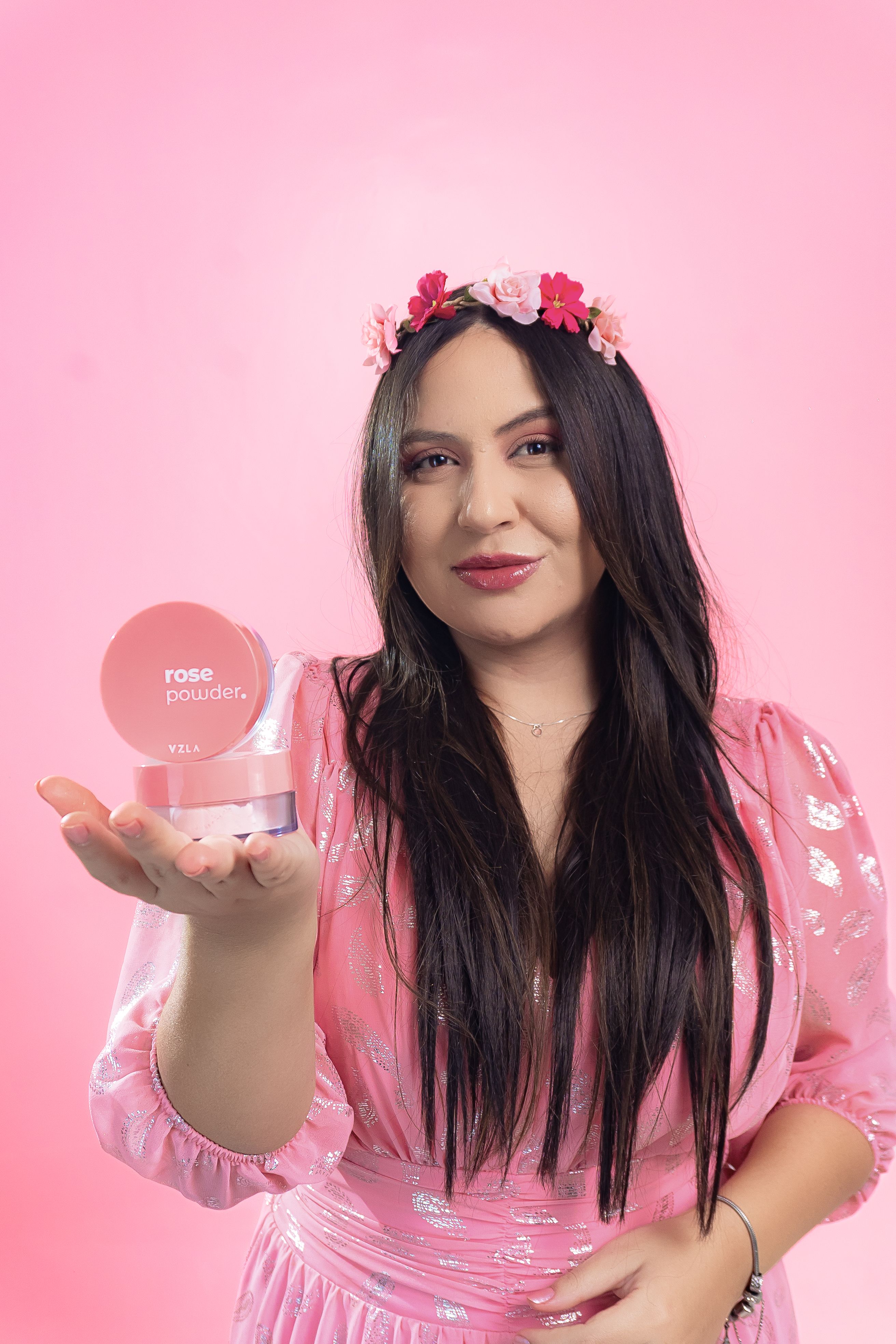 Charming woman in pink dress with floral headband presenting rose powder product.