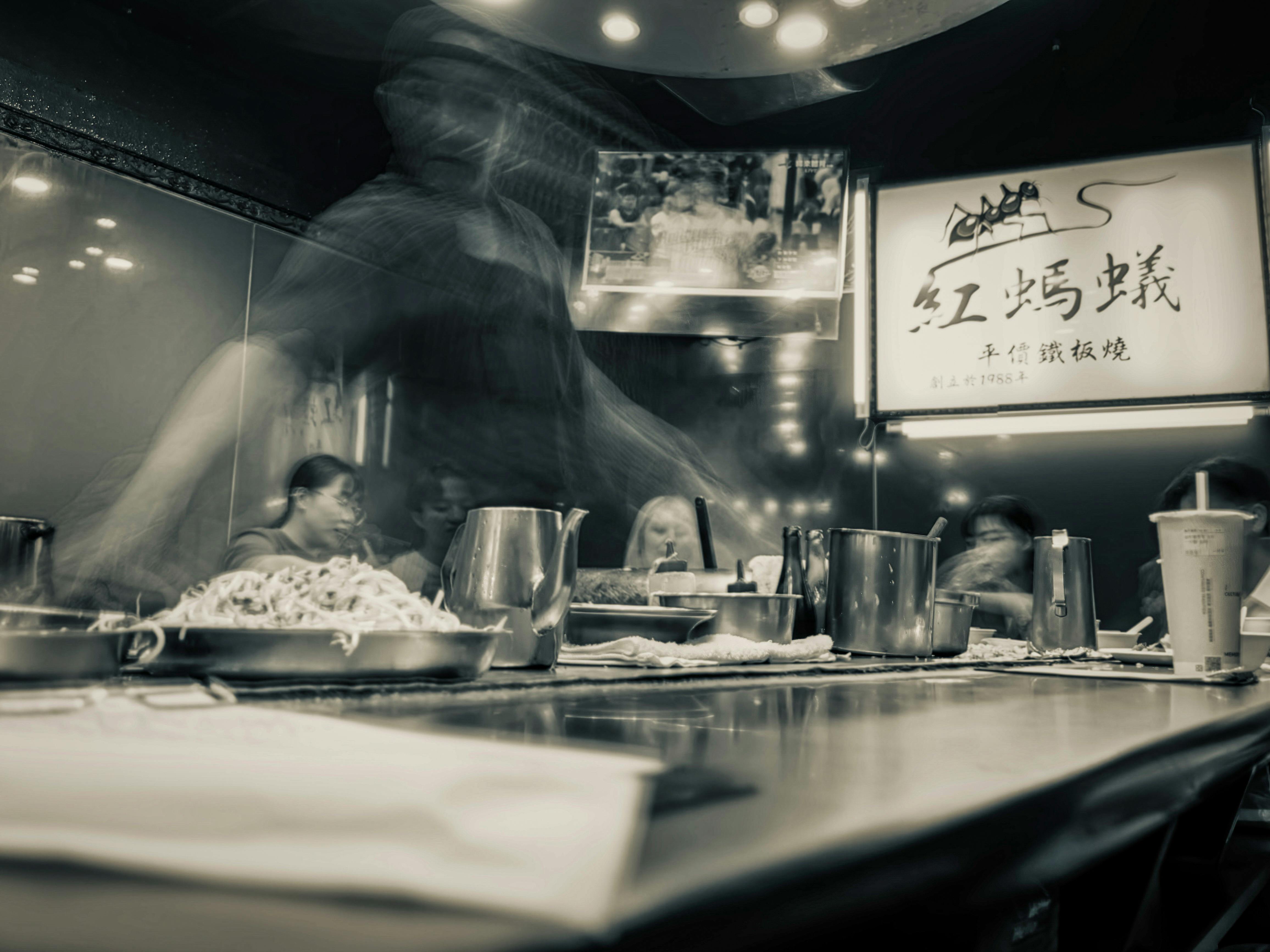 Long exposure shot capturing bustling dining scene in a Taipei City restaurant with ambient lighting.