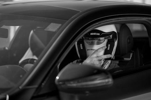 A person in a racing helmet sits in a high-performance sports car, making a victory gesture.