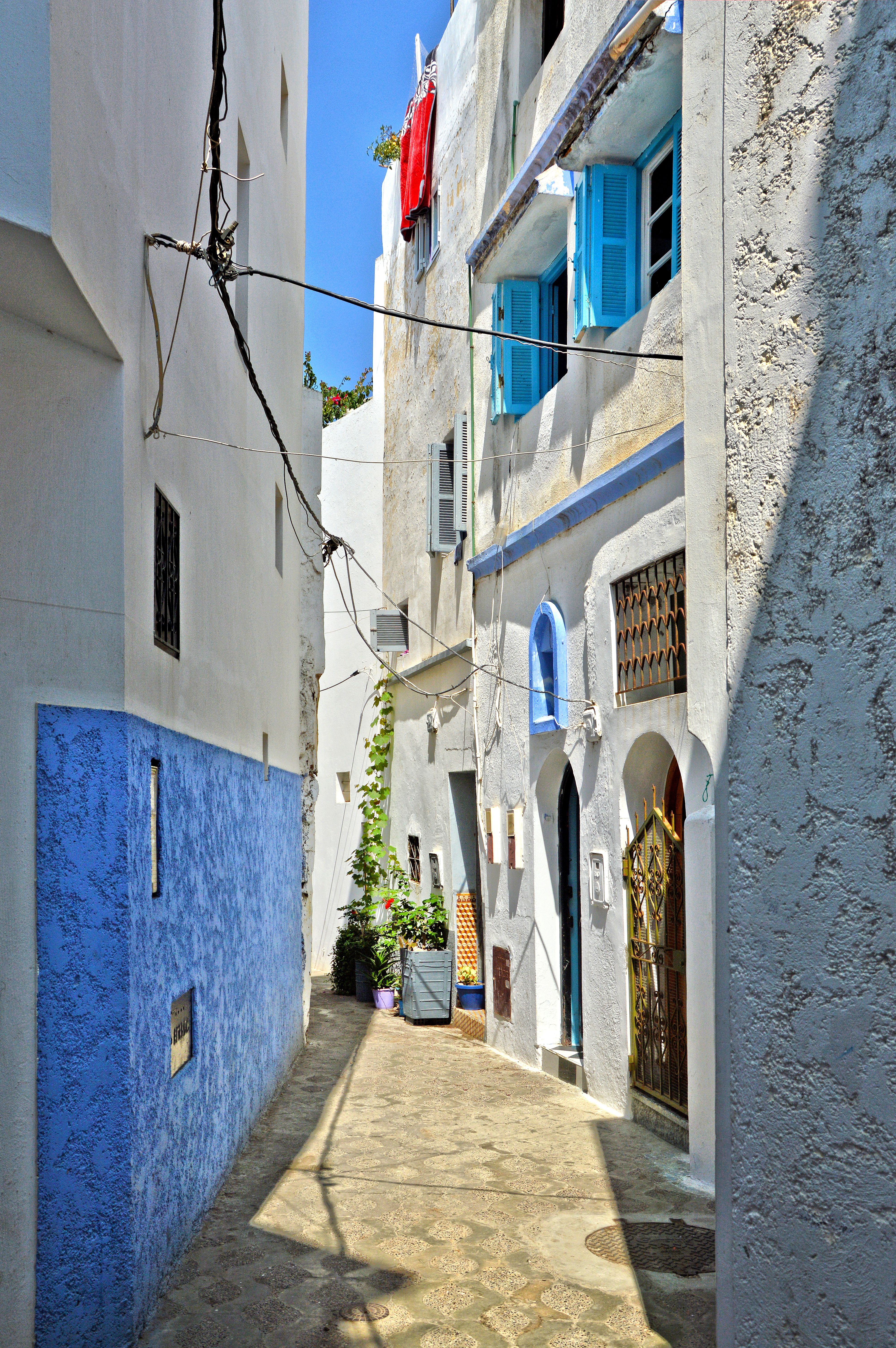 Explore a picturesque narrow alleyway adorned with blue accents and framed by distinctive Mediterranean architecture.