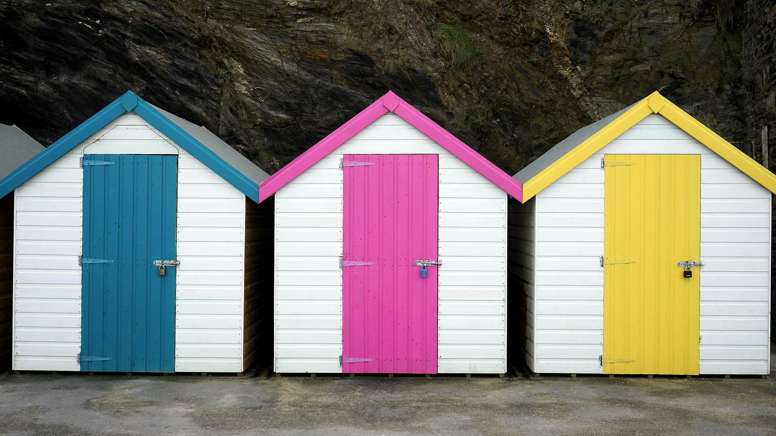 Three white huts with blue, pink and yellow doors