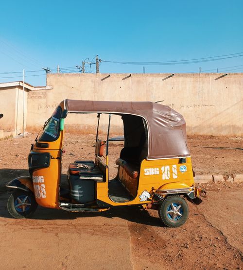 Free A vibrant yellow auto rickshaw parked under a clear blue sky on a sunny day. Stock Photo