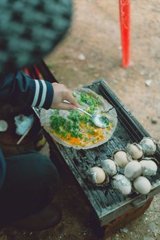 Close-up of preparing Vietnamese rice pancake and grilled eggs on a charcoal stove.