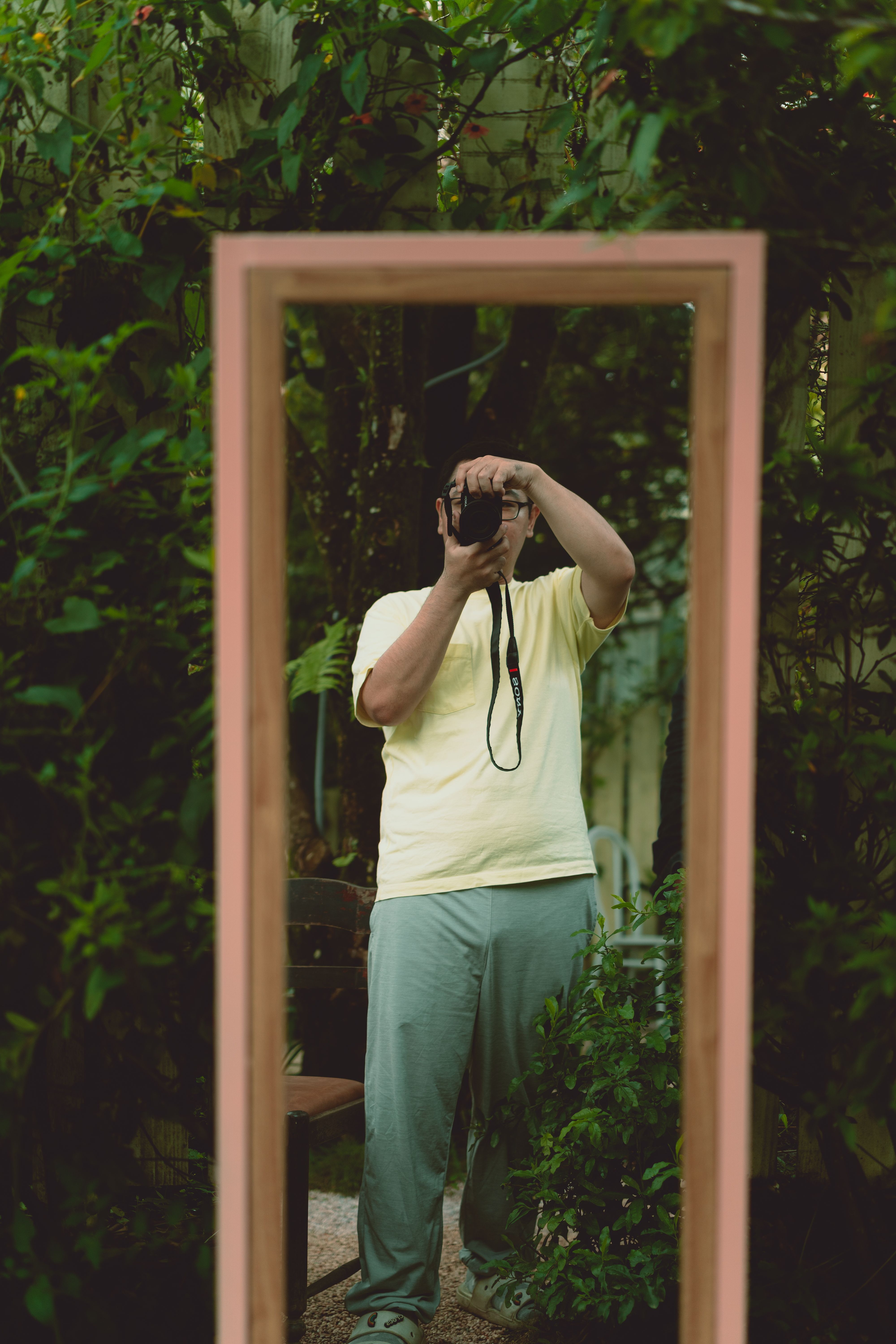 Asian man taking a selfie with a camera in a park using a mirror reflection.