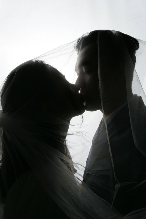 Free Silhouette of an embracing couple kissing beneath a veil, evoking a romantic wedding feeling. Stock Photo