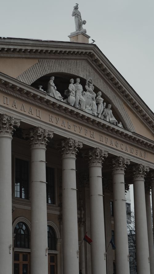 Free Neoclassical building facade featuring columns and sculptures under a cloudy sky. Stock Photo