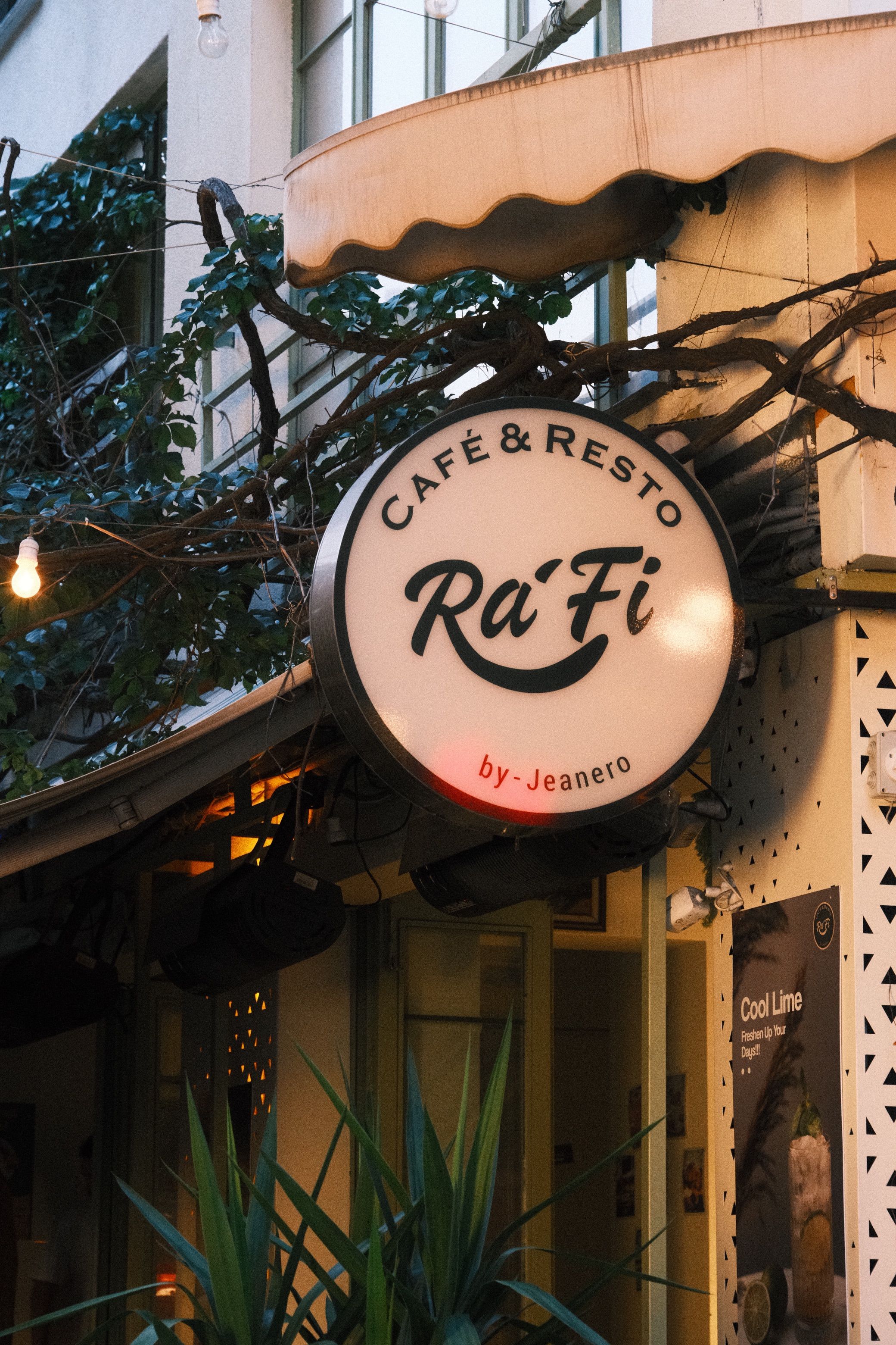 Cozy urban café entrance with prominent 'Rafi' sign and lush greenery.