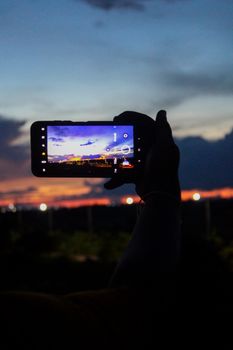Silhouette of a hand holding a smartphone capturing a vibrant sunset in Odisha, India.