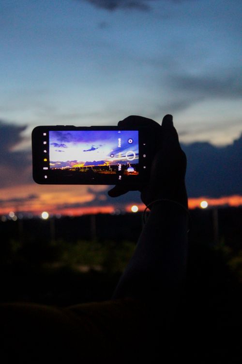 Free Silhouette of a hand holding a smartphone capturing a vibrant sunset in Odisha, India. Stock Photo