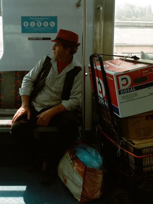 Free Man wearing red hat sits on train with boxes. Urban transit moment captured. Stock Photo