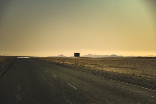 A serene view of an empty road stretching through a desert at sunset with distant mountains.