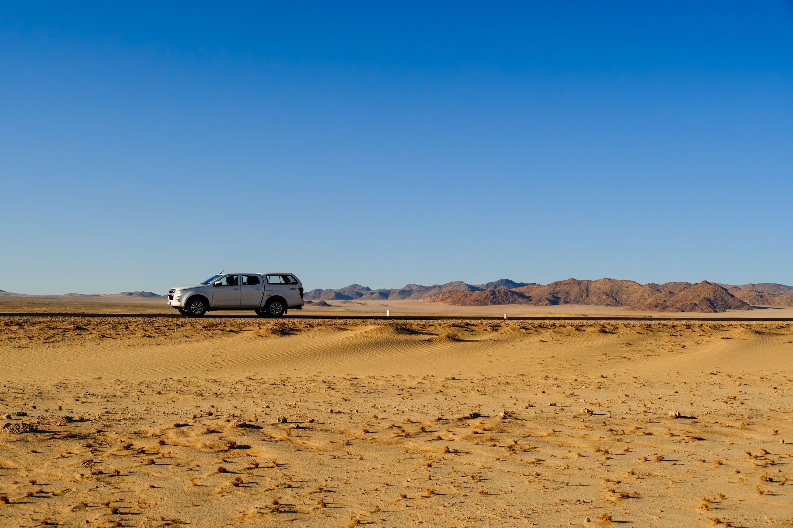 Lone SUV crossing a remote desert road with mountains behind