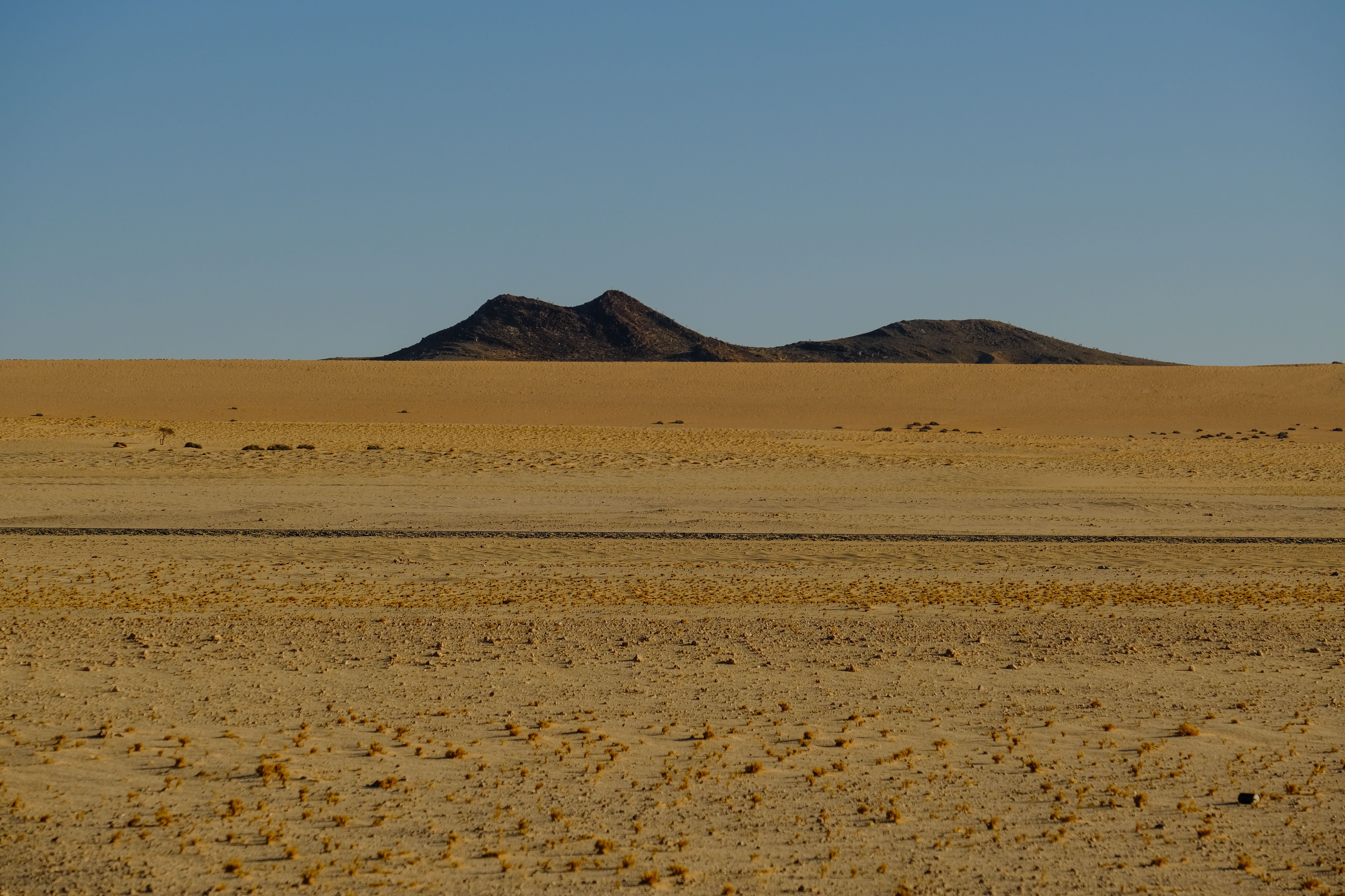 A remote desert landscape with distant hills under a clear blue sky.