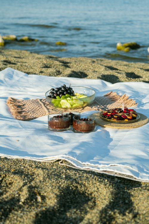 Free A serene beach picnic with fruits, cakes, and ocean view. Perfect summer escape. Stock Photo