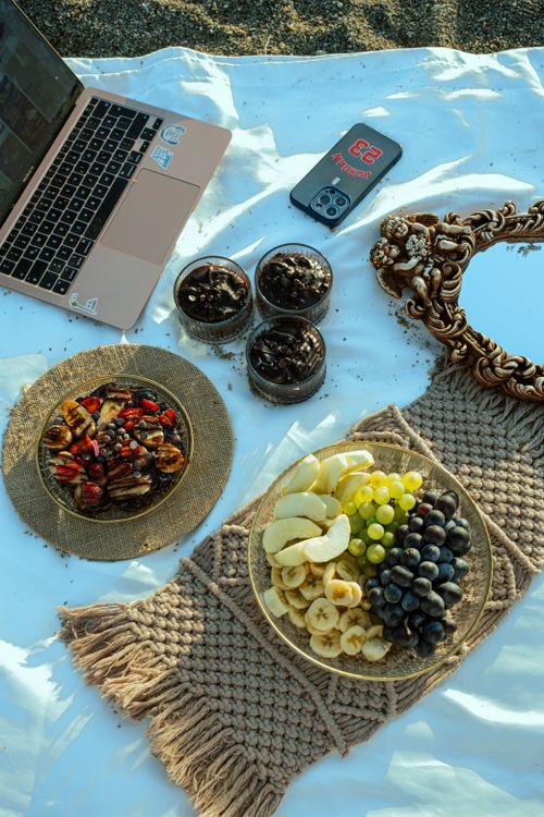 Free Elegant outdoor picnic setup with a laptop, mirror, fruit platter, and dessert jars. Stock Photo