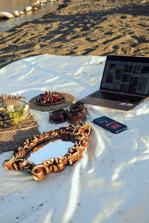 Free Stylish beach picnic setup with desserts, laptop, and decorative mirror on sandy beach. Stock Photo