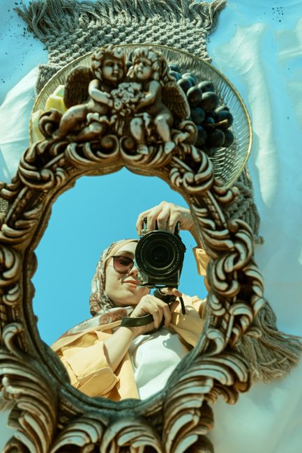 A woman captures her reflection in an ornate decorative mirror outdoors.