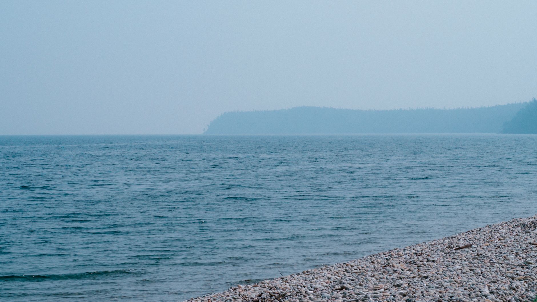 Peaceful view of Lake Baikal's shoreline with clear blue waters under a summer sky.