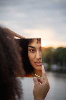 Artistic portrait of a woman using a mirror to reflect the sunset in Hamburg.