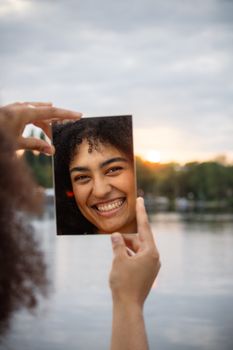 A woman smiles at her reflection in a mirror, set against a serene sunset view in Hamburg.
