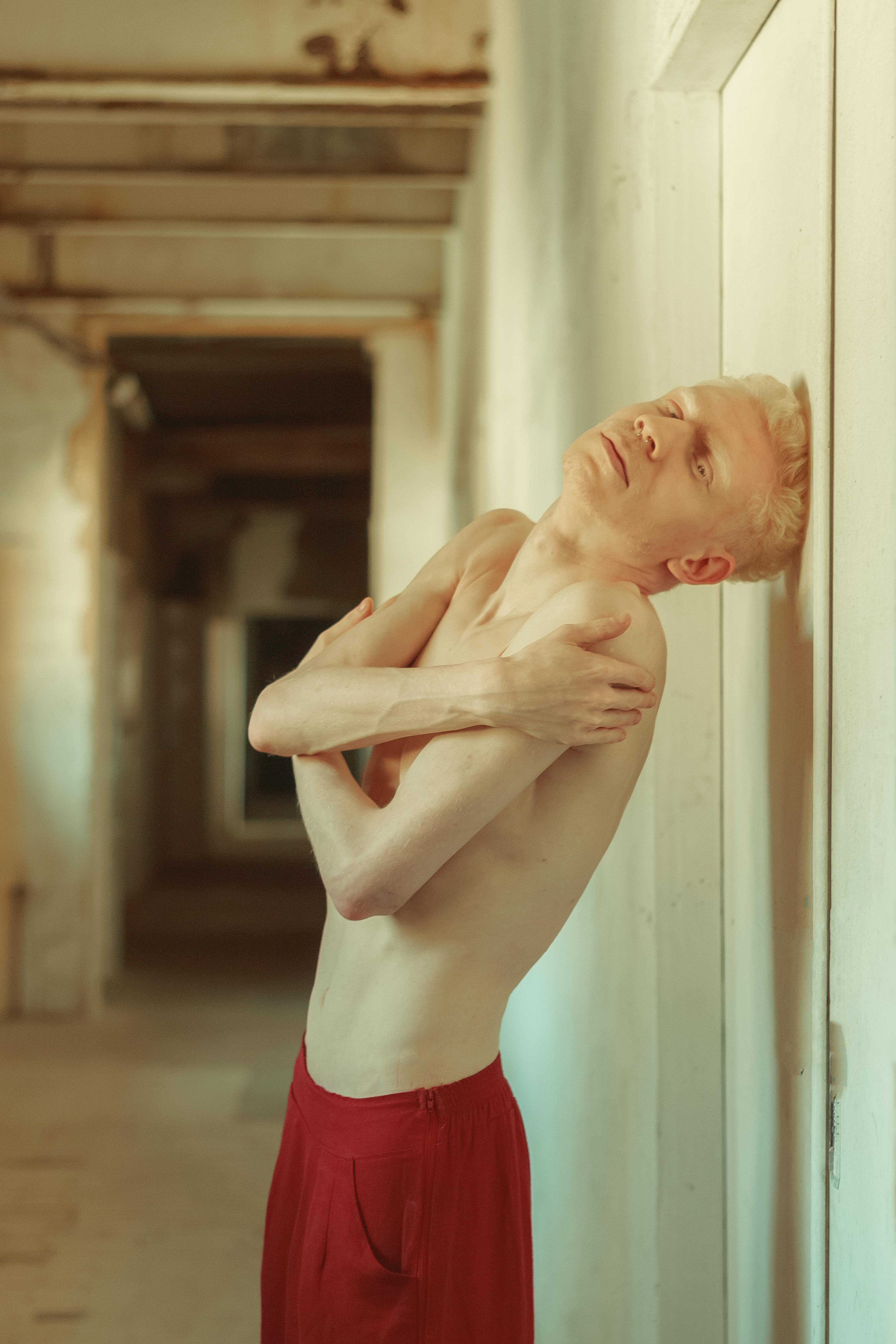 topless man wearing red shorts leaning on white wall