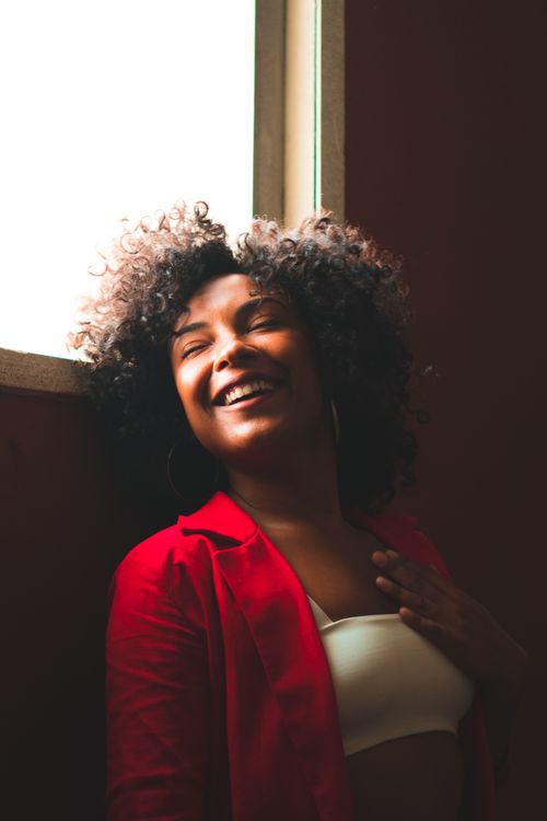 Free A happy woman with curly hair smiles confidently, lit by soft natural light. Stock Photo