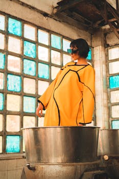 Model in yellow outfit posing in an industrial space with vibrant windows. Fashion-forward and modern.