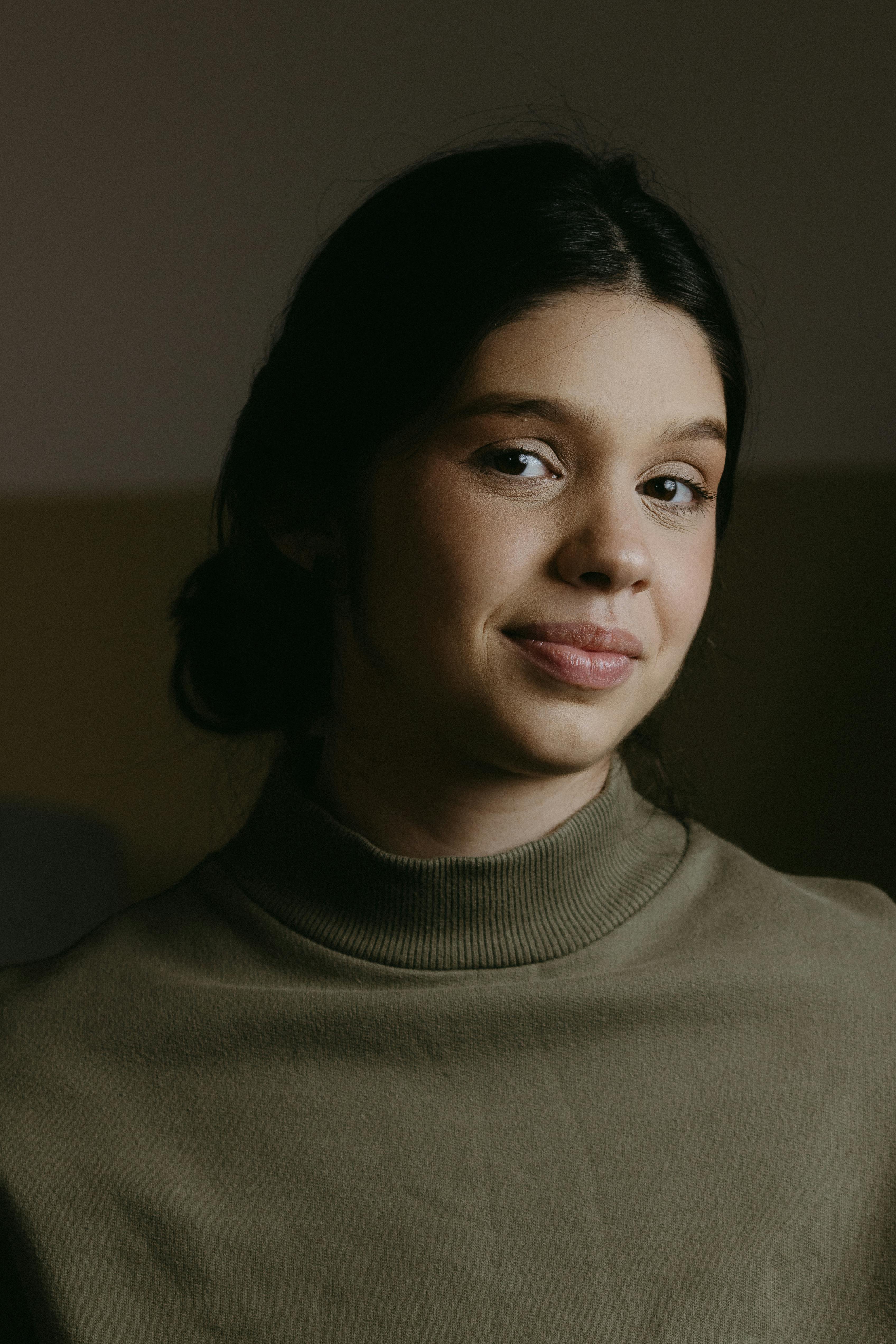 A serene portrait of a young woman wearing a turtleneck sweater indoors, showcasing natural beauty.
