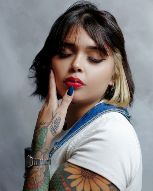 Free Portrait of a tattooed woman with vibrant makeup posing in a studio setting, showcasing style and expression. Stock Photo