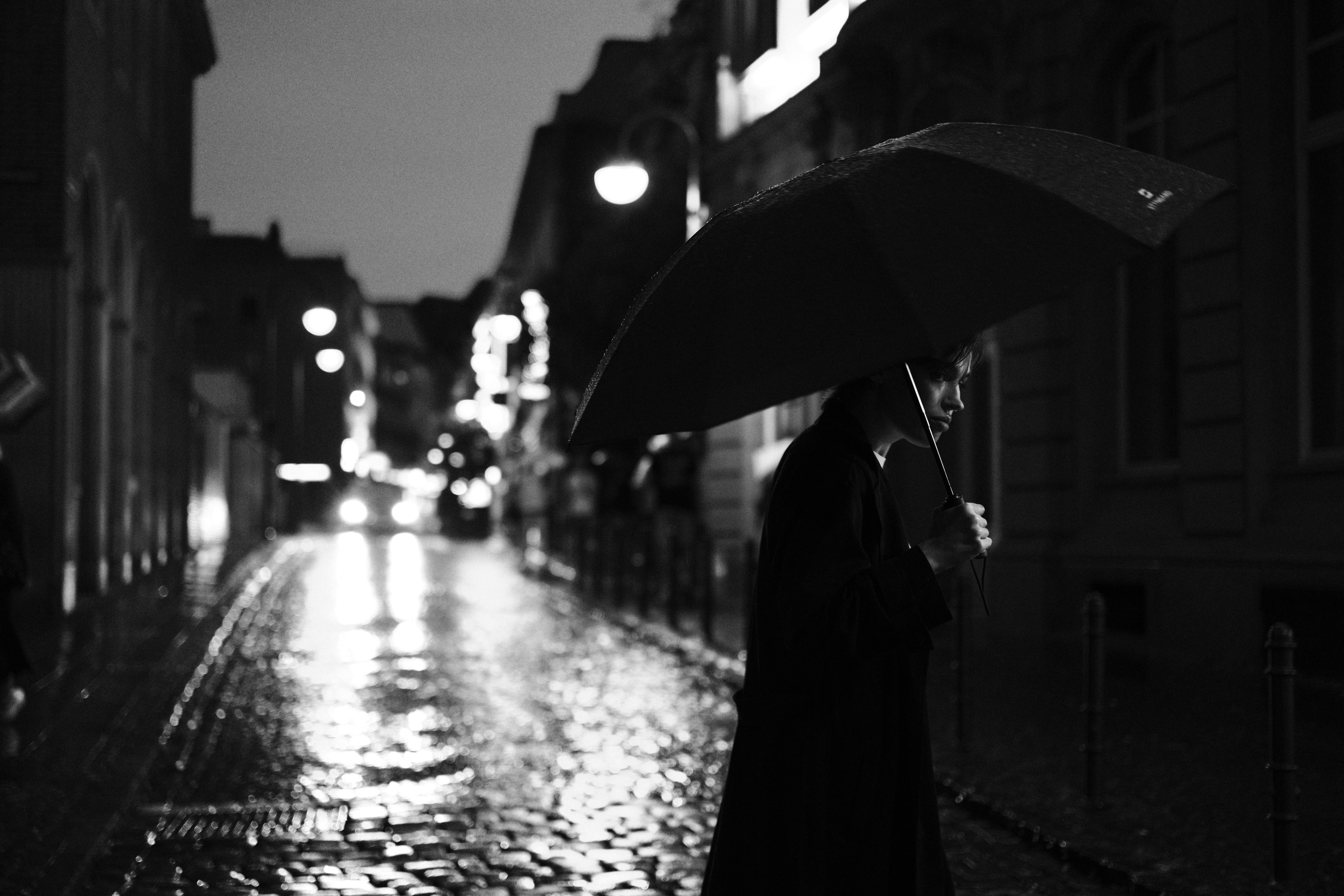 Black and white photo of a person with an umbrella on a rainy night street in Cologne.