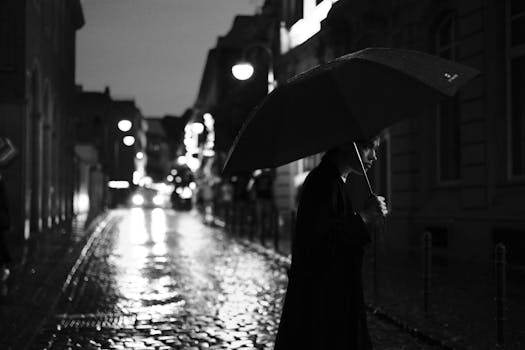Black and white photo of a person with an umbrella on a rainy night street in Cologne.
