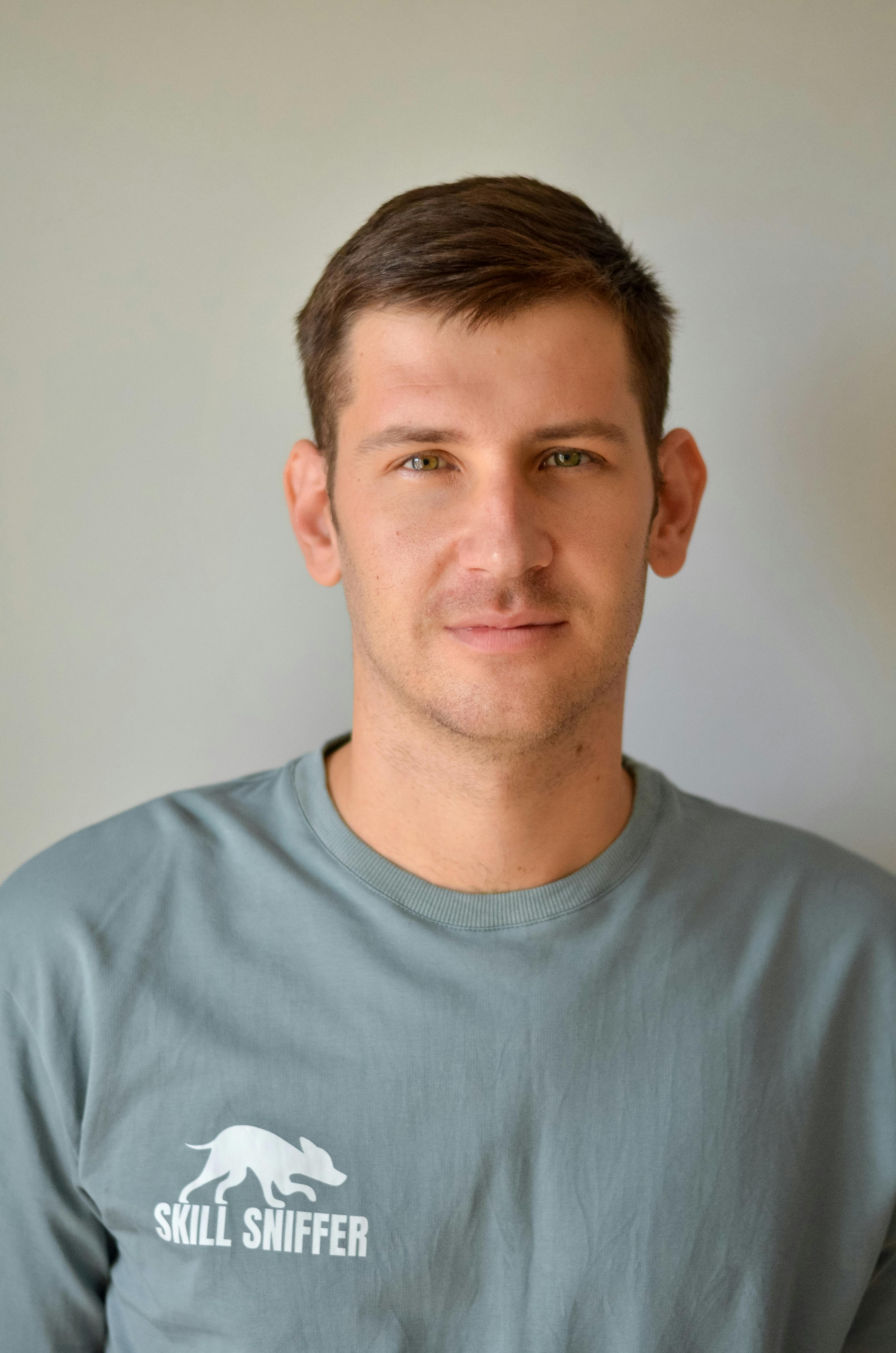 A professional portrait of a young man in a casual outfit with thoughtful expression.
