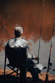 Man sits by a lake fishing, enjoying the tranquility of a serene autumn day.