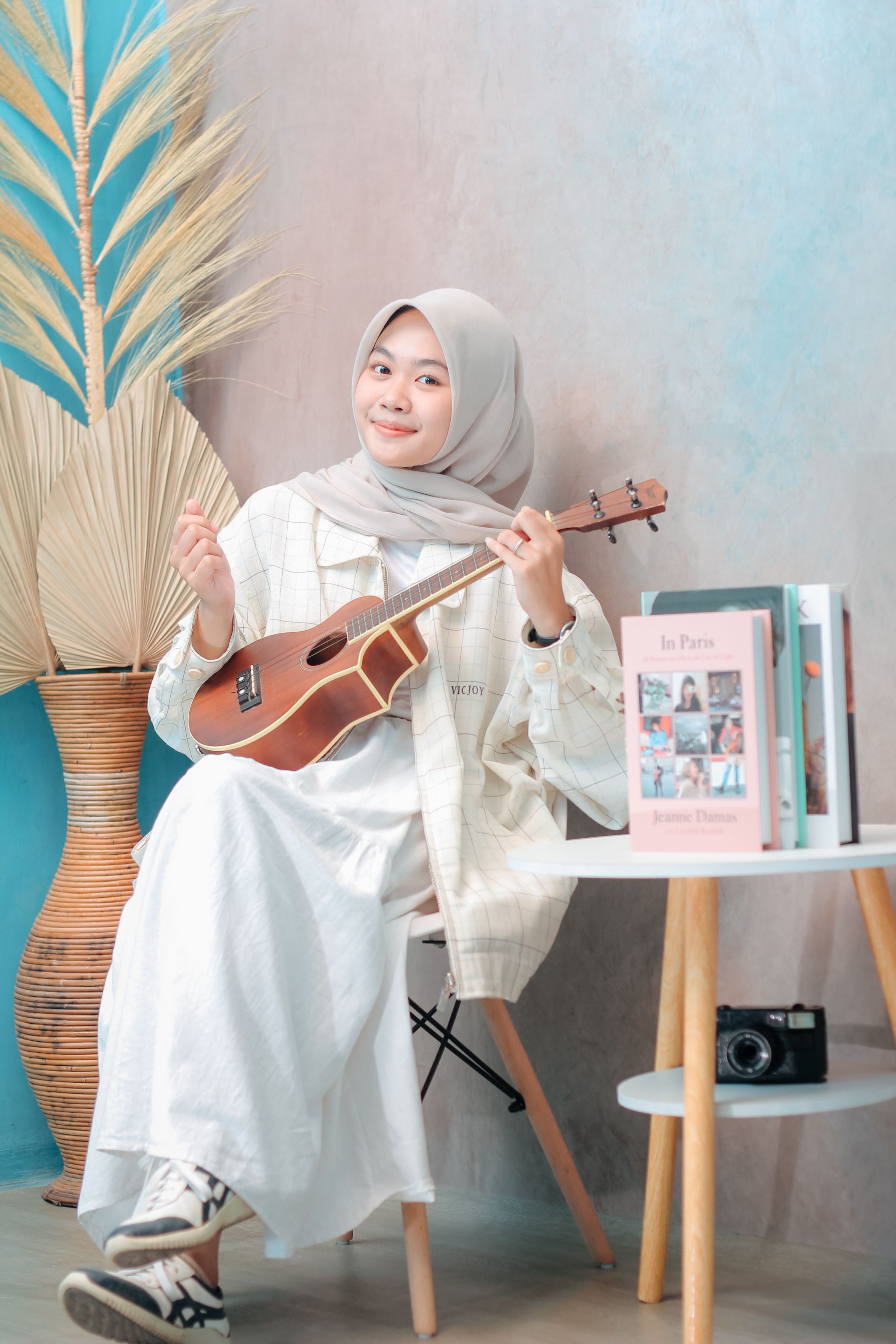 Woman in casual attire plays ukulele indoors, enjoying a relaxed moment.