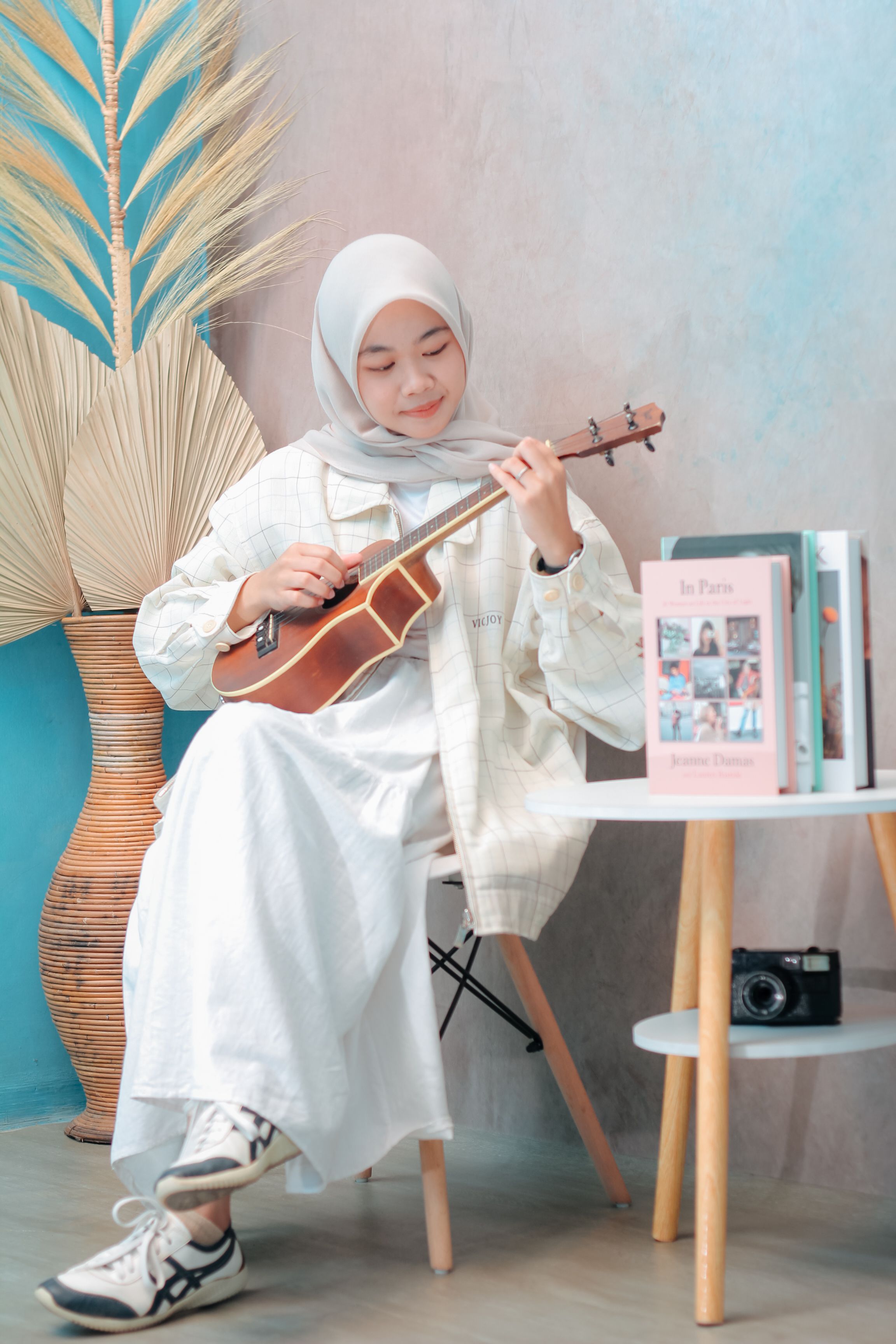Young woman in a hijab playing ukulele inside, expressing creativity and enjoyment.