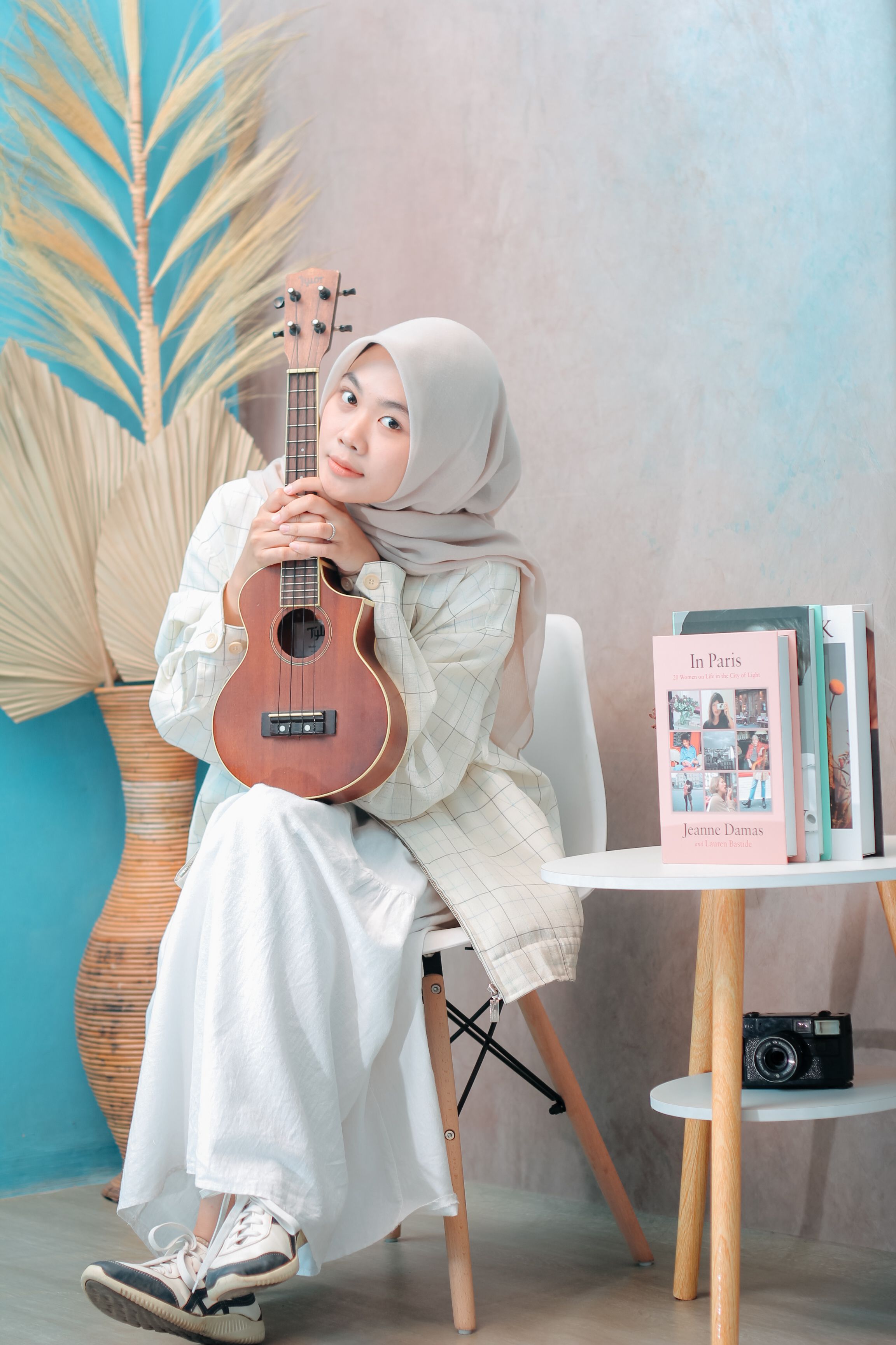 A young woman in a fashionable outfit poses indoors with a ukulele, adding a musical and artistic vibe.