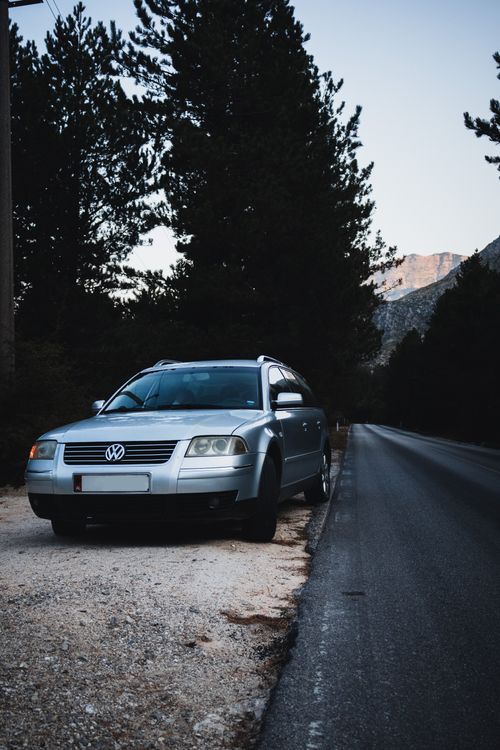 Free A vintage car parked on a serene road lined with pine trees in Vlora, Albania. Stock Photo
