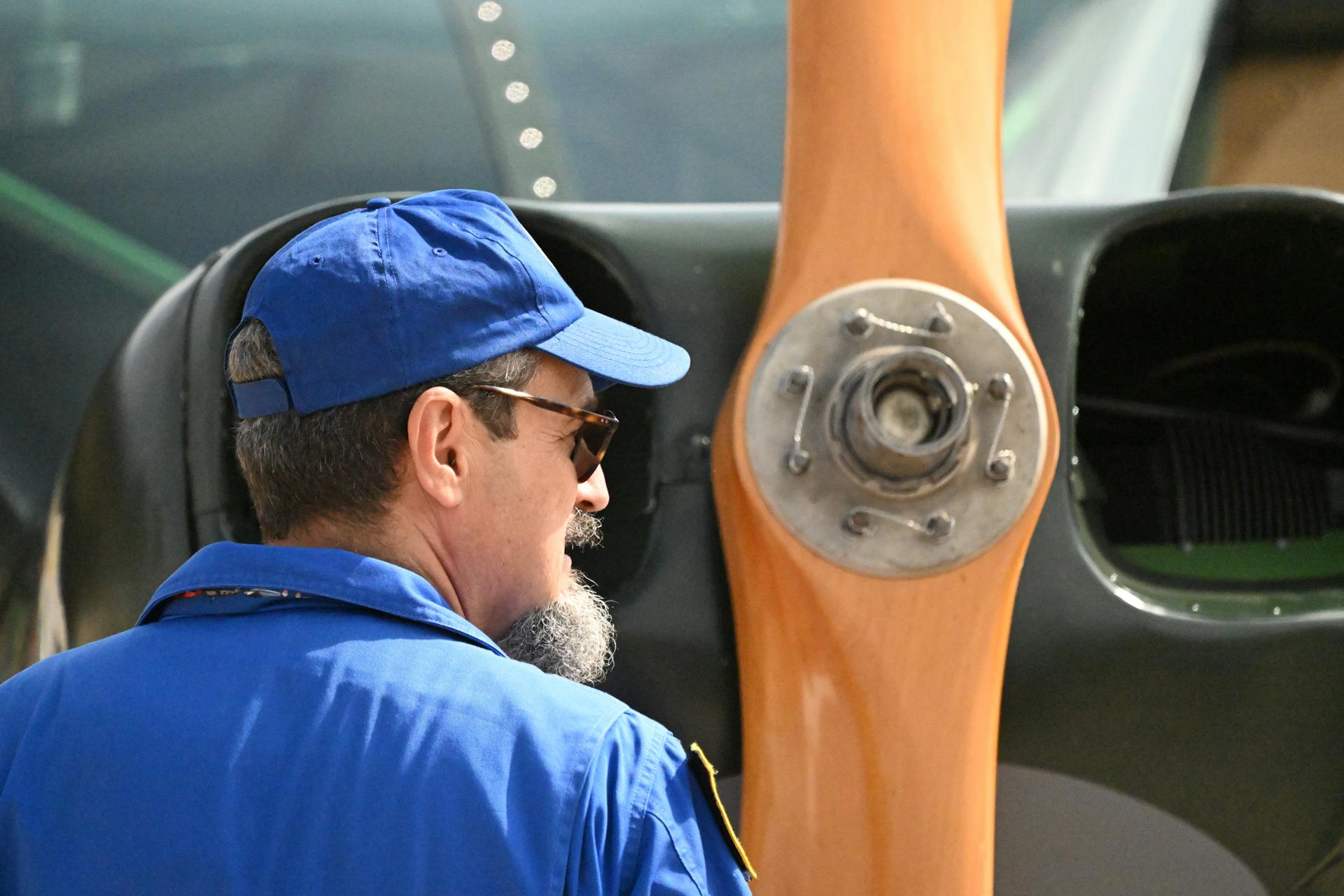 Man in blue inspecting a wooden propeller of a vintage aircraft outdoors in Madrid.