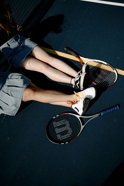 Two women resting on a tennis court with rackets, enjoying leisure outdoors.