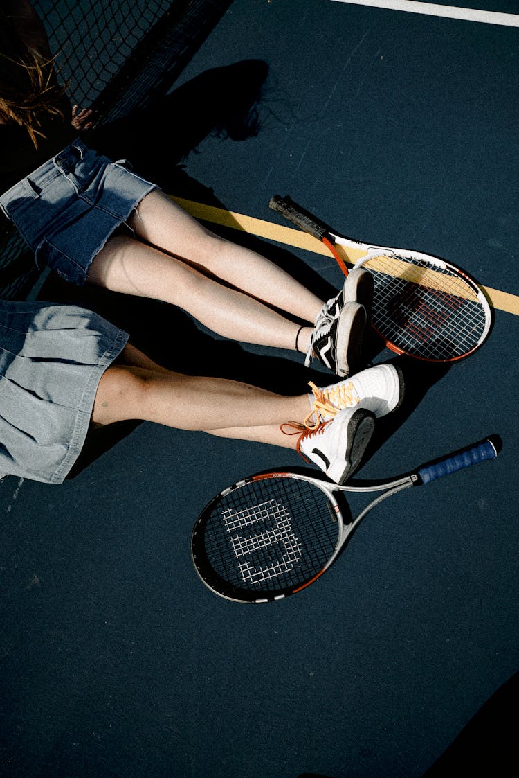 2 Women Sitting On Tennis Court Besides 2 Wilson Tennis Rackets