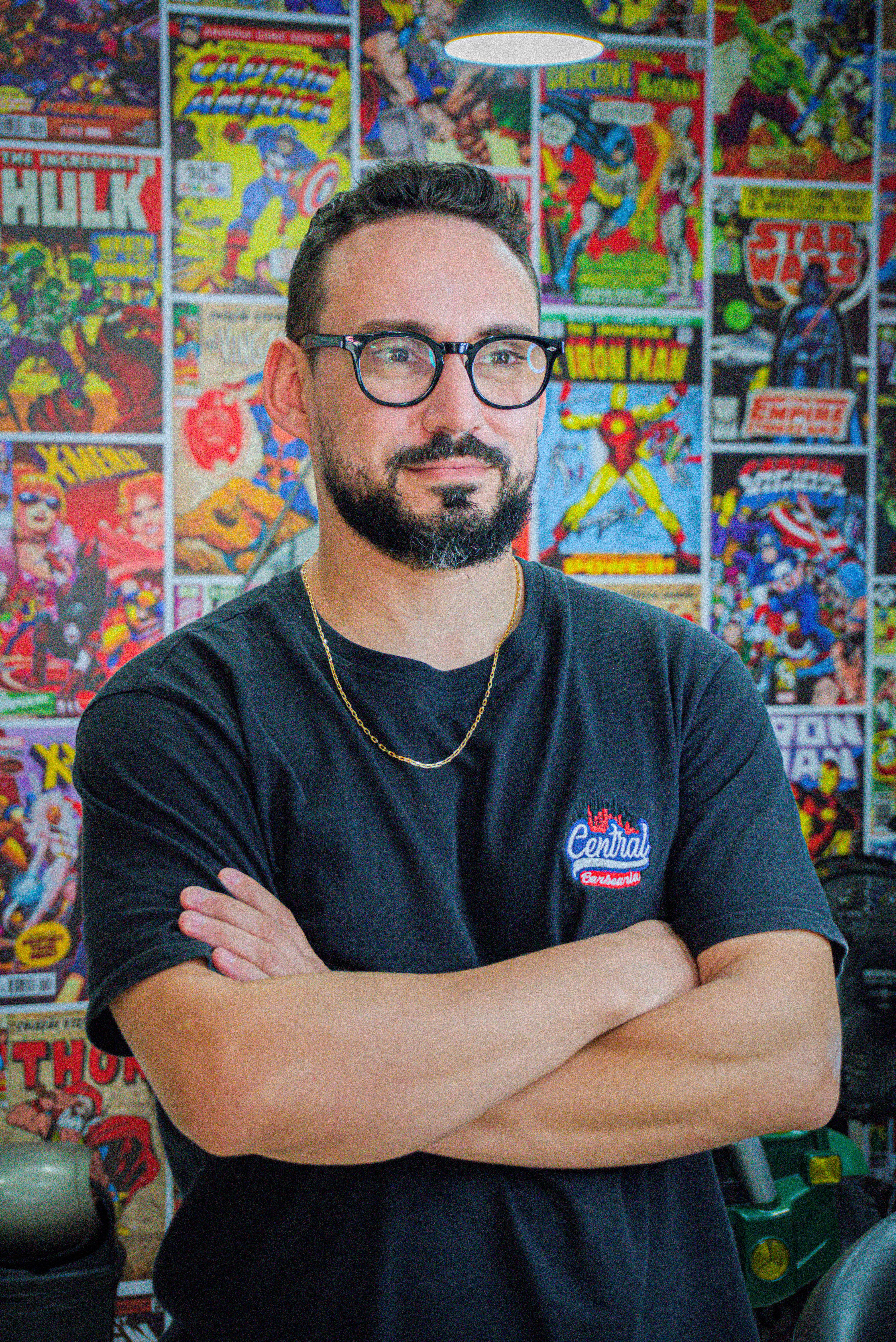 Portrait of a man with glasses and beard standing confidently in front of a comic book wall in Jundiaí, Brazil.