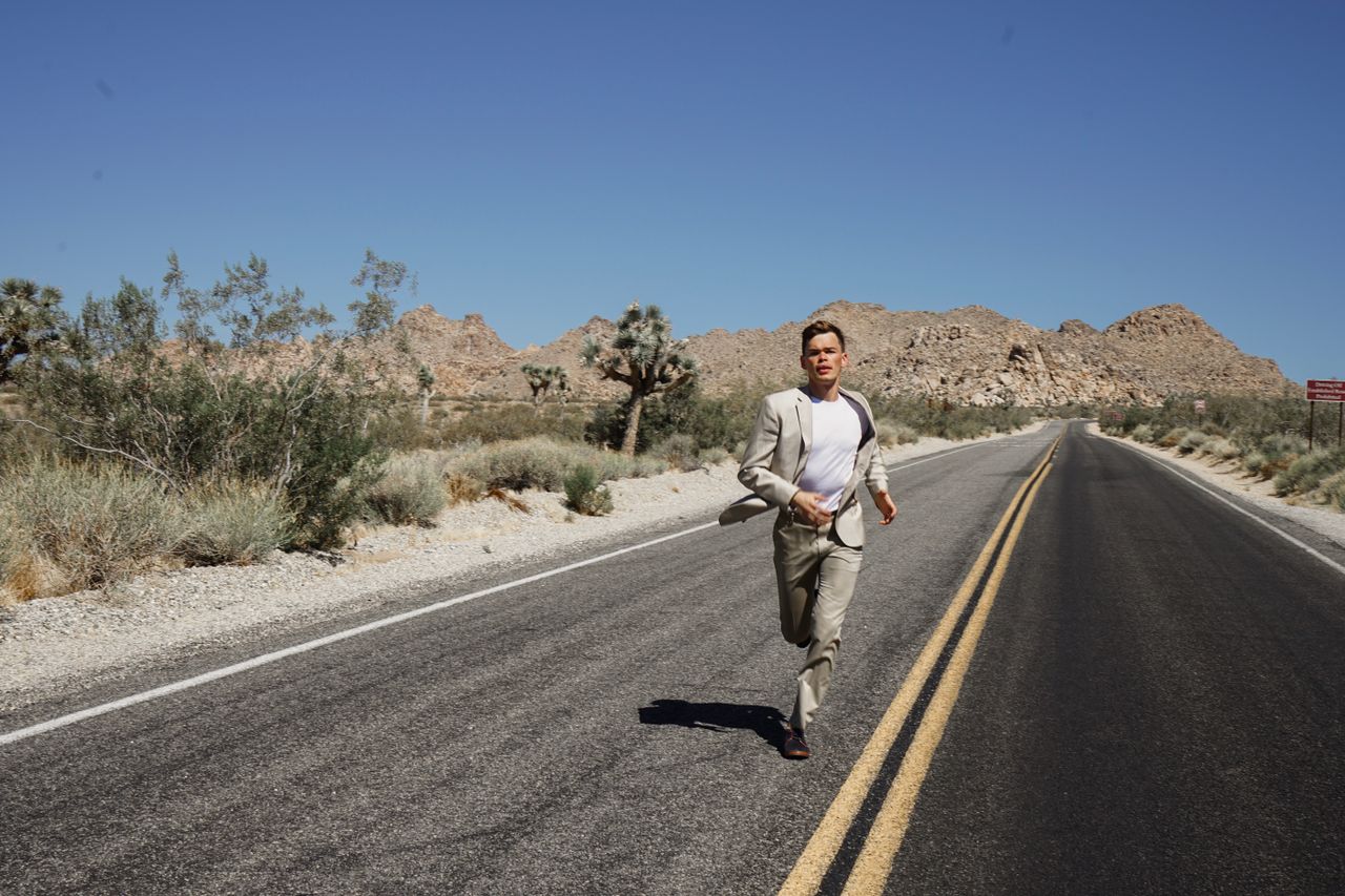 a man in a suit running on an empty desert road surrounded by mountain