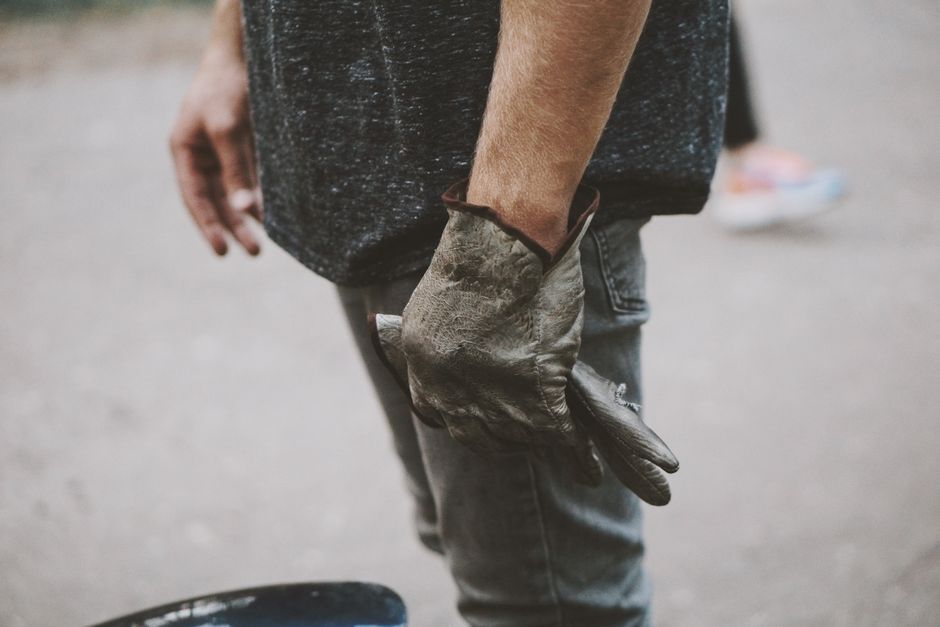 Close-up of a man wearing gloves, standing on a pavement in an urban setting.