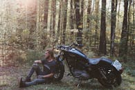 阳光明媚的森林里，一名男子在摩托车旁放松身心，享受大自然