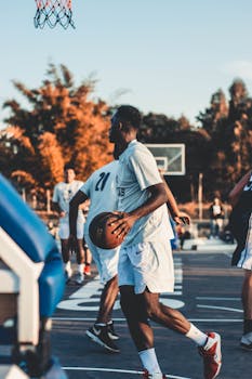Group of men playing basketball outdoors during sunset, showcasing teamwork and action.
