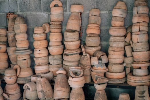 An array of handmade clay pottery pieces stacked against a cement wall, showcasing rustic craft.